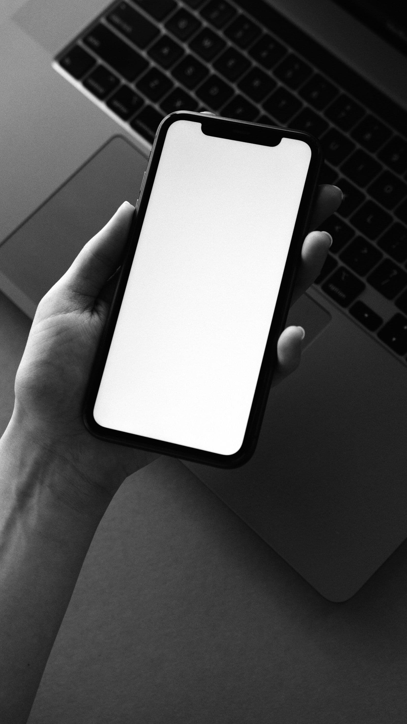 A hand holding a smartphone with a blank screen above a laptop keyboard